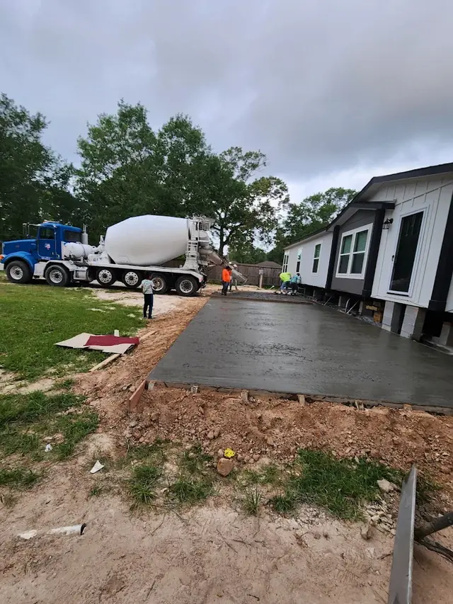 Ready mix truck pouring a driveway slab next to a home